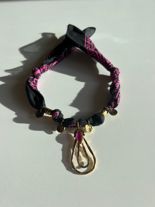 Black and pink bandana charm necklace with decorative elements on a light gray background